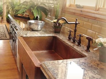 Hammered copper farmhouse sink set into a speckled granite counter with a bronze faucet