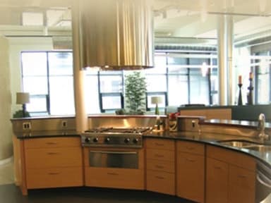 Curved kitchen island with a dark countertop, wood cabinets and a stainless steel range hood in a loft