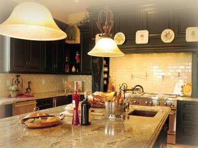 Kitchen island with a granite countertop under two pendant lamps, dark cabinets and a cream tile backsplash